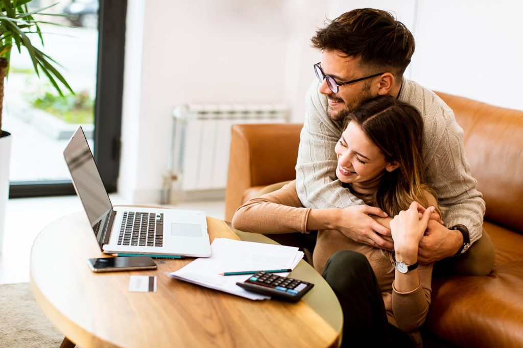 Happy couple embracing while working on finances with a laptop and documents on a coffee table