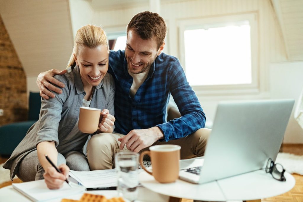 Smiling couple working together at home with a laptop, documents, and coffee mugs