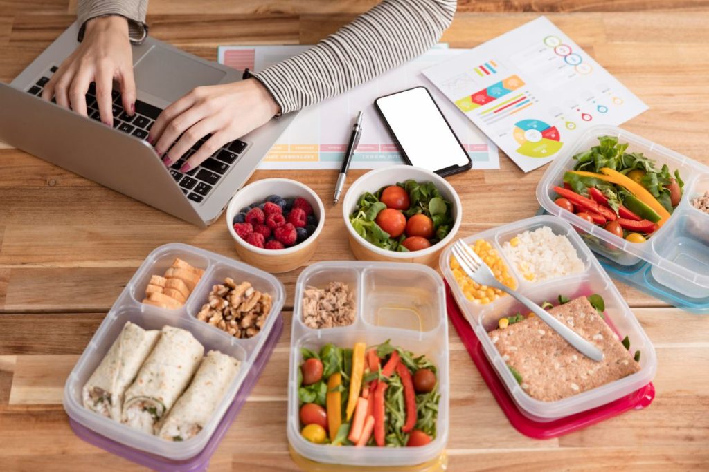 Healthy meal prep containers while a person works on a laptop at home